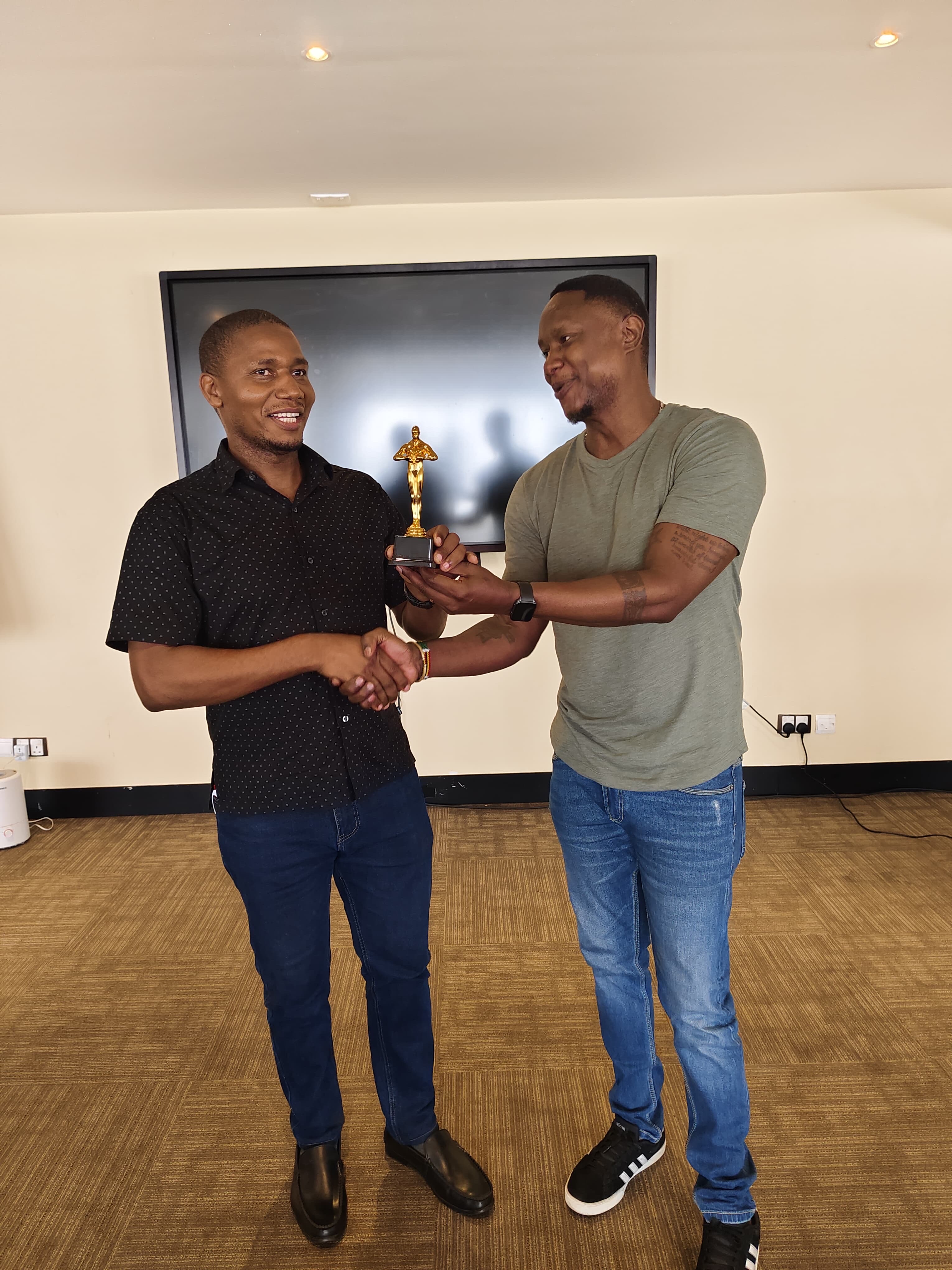 A participant receiving a gold trophy and handshake at the close of a training